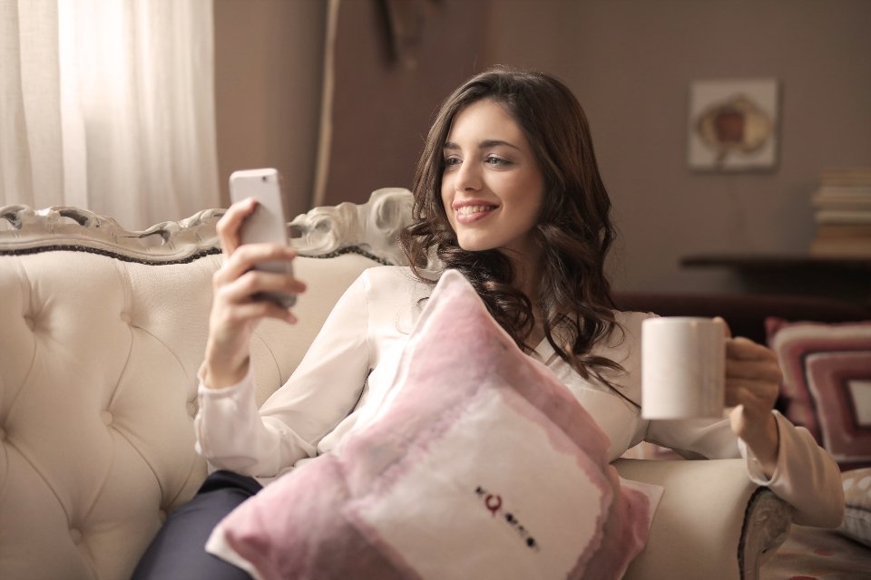 Woman smiling at her phone with a cup of coffee